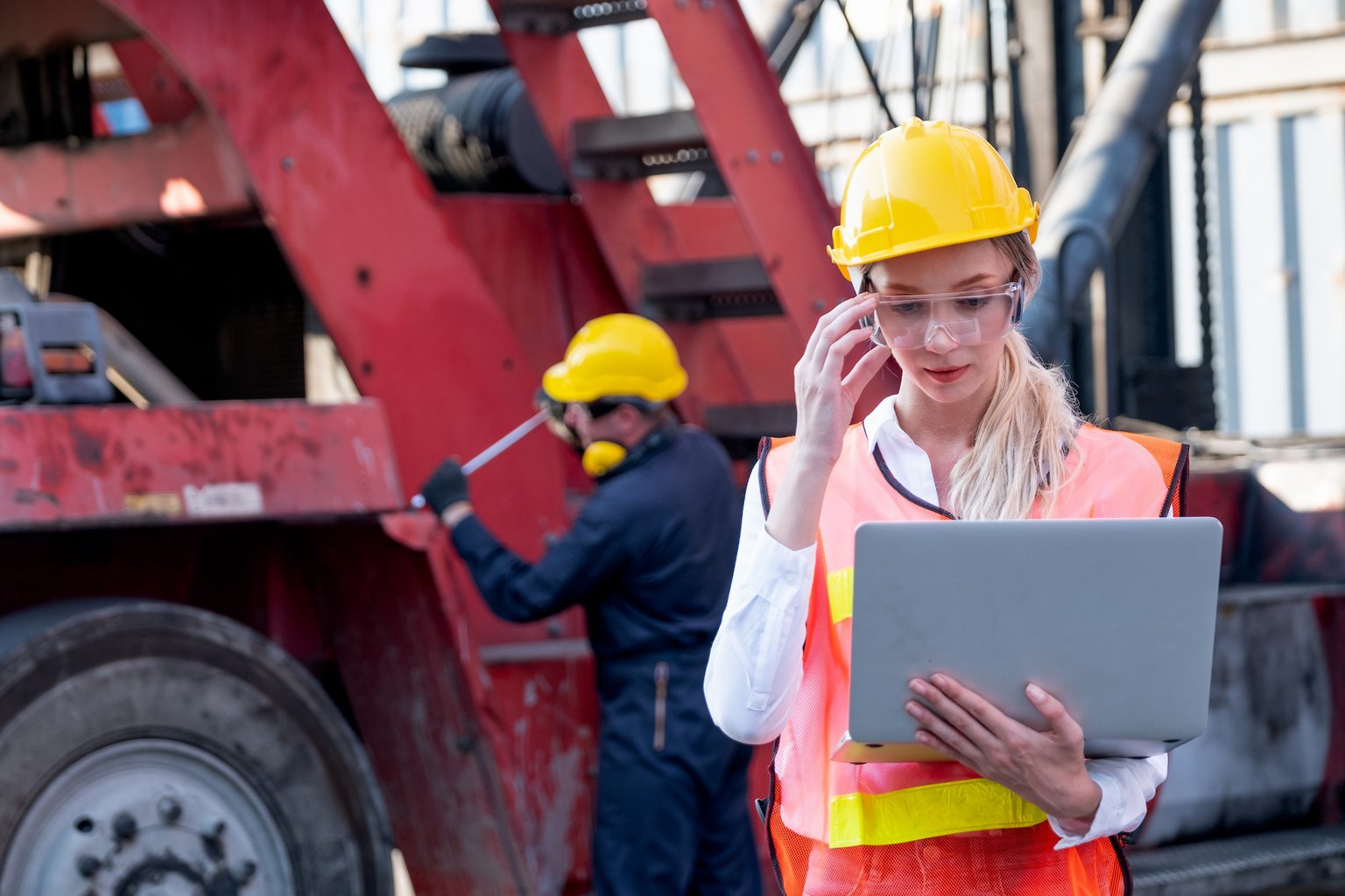 Pretty foreman woman or worker stand with touch her safety eye glasses and holding laptop